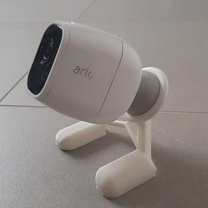 Op de afbeelding: Een witte Arlo-beveiligingscamera gemonteerd op een witte kunststof standaard. De camera heeft een zwarte lens en een witte basis.