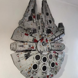 May include: A large, gray and red LEGO Millennium Falcon spaceship model, built and mounted on a wall.