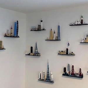 Puede incluir: Una pared blanca con 11 estantes negros que muestran paisajes urbanos en miniatura de Lego. Los modelos de Lego incluyen la Torre Eiffel, el Empire State Building, el London Eye y la &Oacute;pera de Sydney.