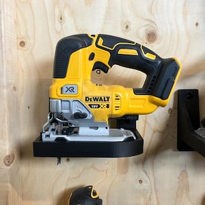 May include: A yellow and black DeWalt 18V XR jigsaw mounted on a black holder. The power tool is attached to a wooden wall. The jigsaw has a silver blade and is designed for cutting various materials.
