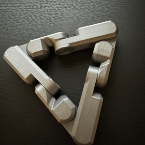 May include: A silver-colored, three-dimensional, interlocking puzzle in the shape of a triangle.