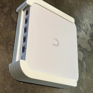 May include: White square-shaped device with a white plastic case and a row of ports on the side. The device has a logo of a stylized letter "U" on the front.