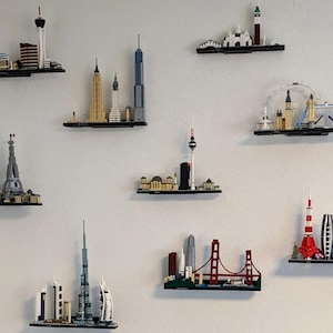 Puede incluir: Una colecci&oacute;n de miniaturas de rascacielos de la ciudad hechos con ladrillos LEGO, expuestos en estantes negros contra una pared blanca. Los rascacielos incluyen monumentos como la Torre Eiffel, el Empire State Building y el Golden Gate Bridge.