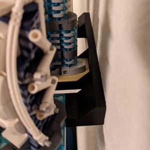 Puede incluir: Un soporte de pared de pl&aacute;stico negro para exhibir un modelo de Lego. El soporte est&aacute; dise&ntilde;ado para sujetar el modelo de forma segura a la pared.