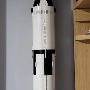 May include: A white and black model rocket with the text "Saturn V" on the side. The rocket is mounted on a black stand.