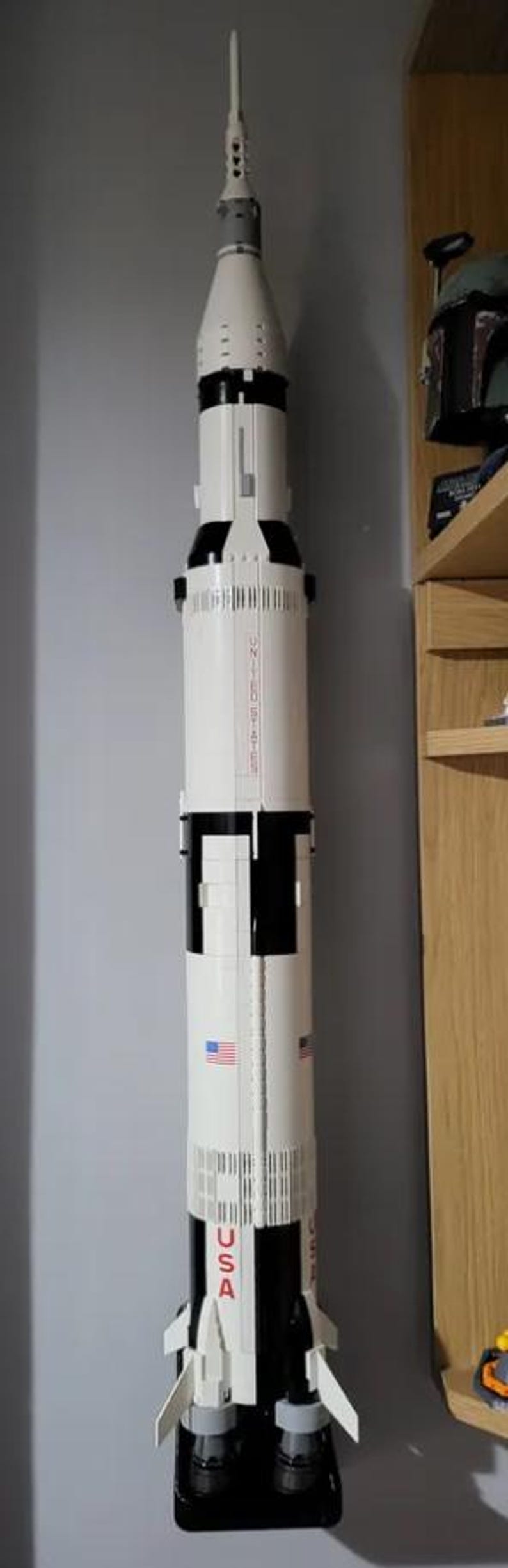 May include: A white and black model rocket with the text "Saturn V" on the side. The rocket is mounted on a black stand.