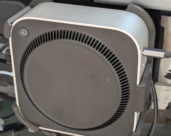 Może przedstawiać: Srebrny i czarny komputer Mac mini z przyciskiem zasilania z przodu. Komputer jest zamontowany na uchwycie ściennym.