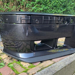 May include: Black plastic car bumper with a rectangular opening in the center. The bumper has a smooth, glossy finish.