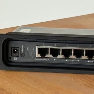 May include: Black network switch with five Ethernet ports, labeled 1 through 5. The front panel includes power and USB ports, and the text "Internet/PoE in" and "LAN" are visible. The device is mounted in a rack.