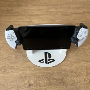 May include: White PlayStation 5 console stand with a black PlayStation logo. The stand has two white controllers attached to the sides.