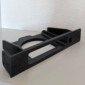 May include: A black, 3D-printed bracket with a circular opening and rectangular frame. The bracket has a textured surface and features several holes and cutouts. It appears to be designed for mounting or support purposes.