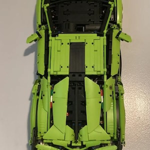 May include: A green Lamborghini Sian LEGO Technic model car with black details. The car is built with LEGO bricks and has a detailed engine and interior.