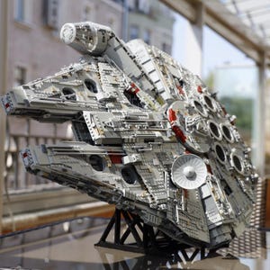 May include: A detailed model of the Millennium Falcon spaceship, built from LEGO bricks. The model is gray and white with red accents and features a detailed cockpit and engine.