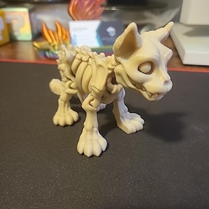 May include: A beige plastic skeletal dog figurine with a detailed bone structure and a toothy grin. The figurine is standing on a black surface.