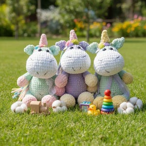 May include: Three handmade crochet unicorn plush toys in pastel colors sit on green grass. Each unicorn has a white body, a colorful mane, and a horn. Toys and cotton balls are scattered around the unicorns.