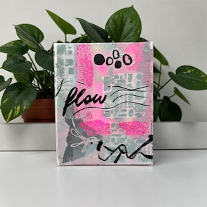 Könnte beinhalten: Ein rechteckiges Leinwandgemälde mit abstrakten Schichten aus leuchtend rosa, salbeigrüner und grauer Farbe. Das Kunstwerk enthält handgemalte schwarze Elemente, darunter das Wort "flow" in Schreibschrift, mehrere ausgefüllte Kreise und Wellenlinien.