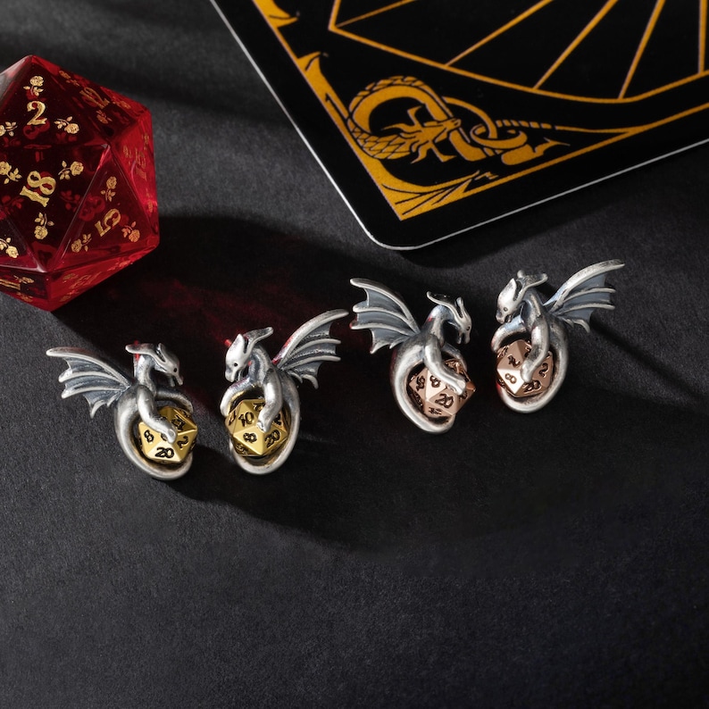 May include: Four silver dragon charms with a gold, copper, and silver dice in their claws. The charms are on a black surface.