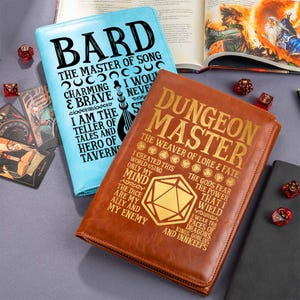 Puede incluir: Dos diarios encuadernados en cuero, uno azul claro con "BARD" y el otro marrón con "DUNGEON MASTER" en letras doradas. Se ven dados y un libro abierto, lo que sugiere un tema de juego de rol.