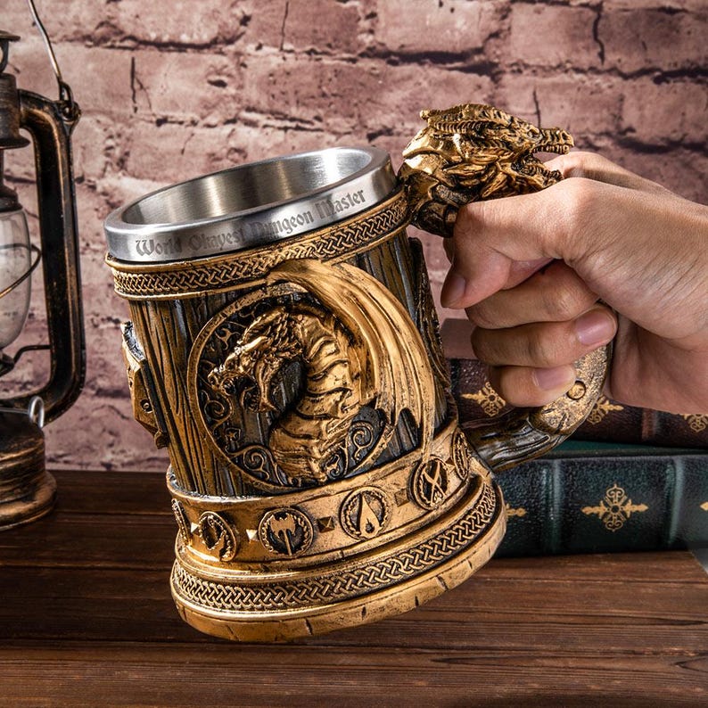 Op de afbeelding: Een gedetailleerde, goudkleurige fantasiebeker met een drakenontwerp. De beker heeft een roestvrijstalen binnenkant en de woorden "World Okayest Dungeon Master" rond de rand. De handgreep is gevormd als een drakenkop.