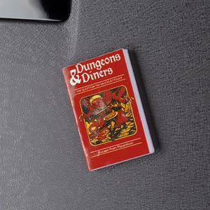 May include: A red and white magnet with the text "Dungeons & Diners" and an illustration of a monster. The magnet also includes the text "The Quest for the Sauces of Power" and "Escape From Flavortown".