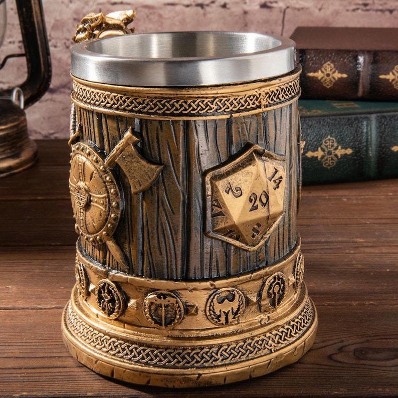 Op de afbeelding: Een gedetailleerde bierpul met fantasiethema, met een metalen rand en handvat. De body heeft een houtnerftextuur met reli&euml;fschild, bijl en dobbelsteenontwerpen. Goud- en bronsaccenten benadrukken de ingewikkelde details, waaronder een decoratieve basis.