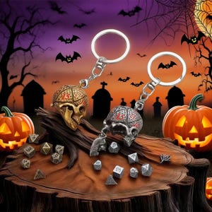 Può includere: Due portachiavi a forma di teschio con anelli argentati, uno dorato e uno argentato, poggiano su una superficie di legno con dadi. Lo sfondo presenta una scena di Halloween con zucche, pipistrelli e un cimitero.