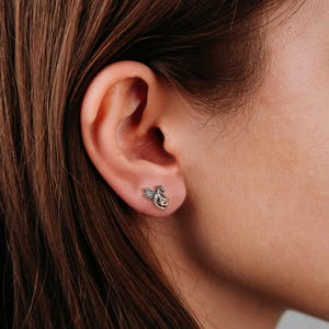 May include: A silver dragon head stud earring with a rose gold accent. The earring is worn in a person's left ear.