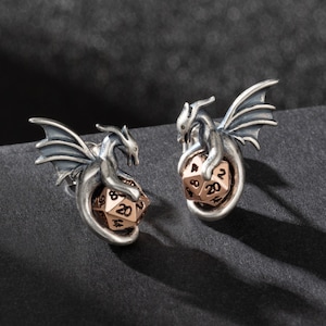 May include: A pair of silver dragon earrings with a rose gold 20-sided die in the center of each dragon.