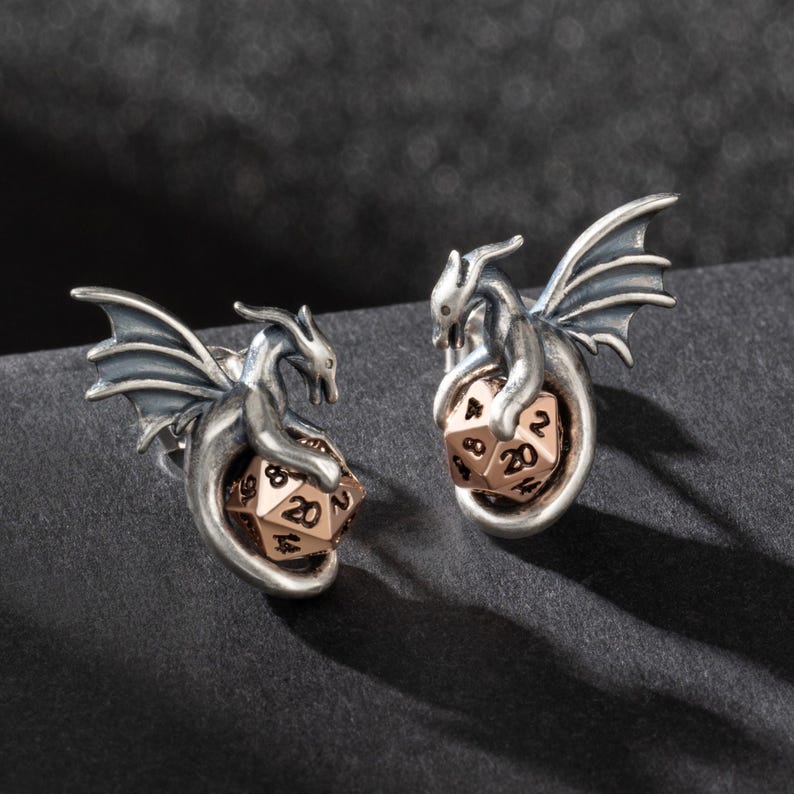 May include: A pair of silver dragon earrings with a rose gold 20-sided die in the center of each dragon.