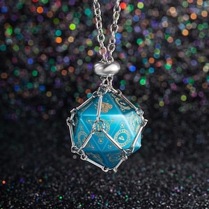May include: A blue and gold D20 dice pendant necklace. The dice is encased in a silver metal cage and suspended from a silver chain. The dice features gold-colored symbols and numbers. The background is a dark, glittery surface.