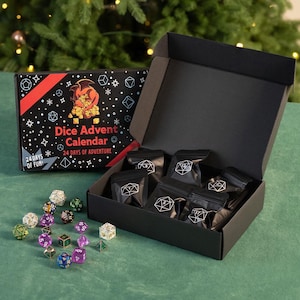 May include: A black box labeled "Dice Advent Calendar" with a red and black design, open to reveal small black bags. Scattered dice in various colors and shapes are on a green surface. The box reads "24 Days of Adventure."
