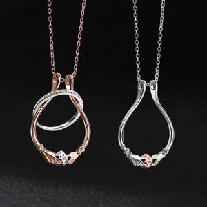 Peut inclure: Deux colliers avec pendentifs. L'un est en or rose avec une torsade argentée et un petit dé tenu par des mains. L'autre est argenté avec un design similaire. Les deux ont des chaînes délicates.