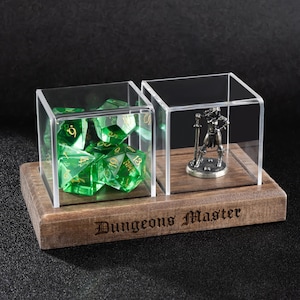 May include: A wooden display case with two clear acrylic cubes. One cube contains green polyhedral dice, the other a silver figurine. The base is engraved with "Dungeons Master".