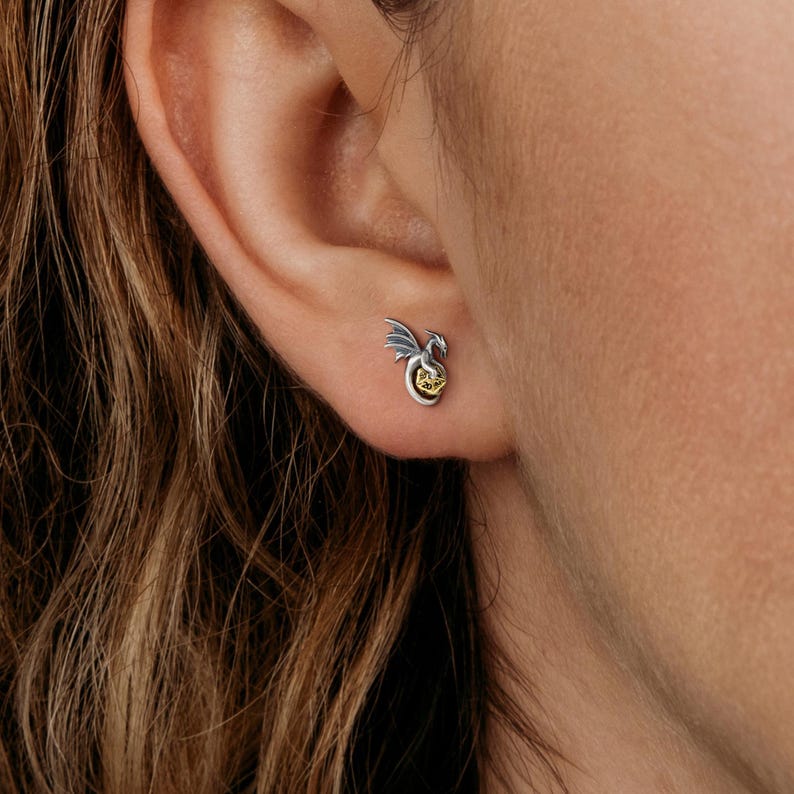 May include: Silver dragon earrings with a gold accent. The dragon is curled around a sphere.