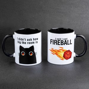 Peut inclure: Deux mugs en céramique blancs avec l'intérieur et les anses noirs. L'un des mugs présente un chat noir avec le texte "I didn't ask how big the room is". L'autre mug affiche "I said I cast FIREBALL" avec une boule de feu et un dé rouge.