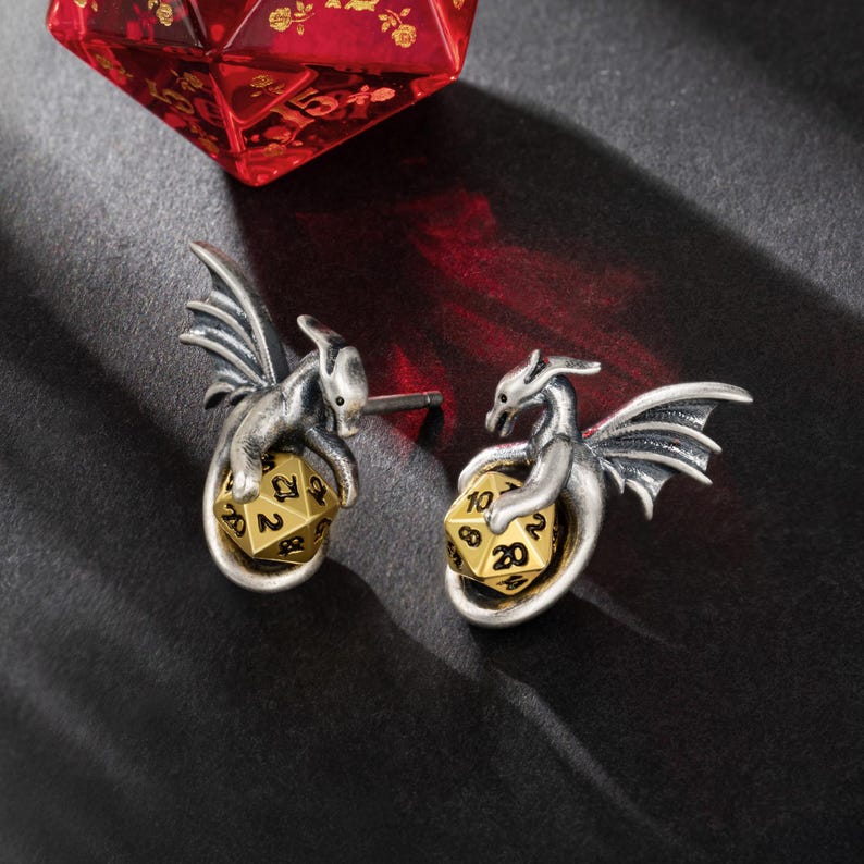May include: A pair of silver dragon earrings with gold 20-sided dice. Each dragon is holding the die in its claws.