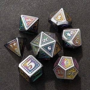 Peut inclure: Un ensemble de sept dés polyédriques métalliques irisés pour jeux de société. Chaque dé présente une bordure argentée et des surfaces chatoyantes colorées avec des chiffres blancs. Les dés sont disposés sur une surface sombre et texturée.