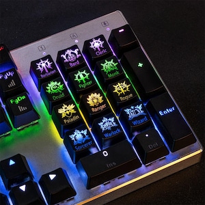 Puede incluir: Primer plano de un teclado para juegos con teclas iluminadas. Las teclas negras tienen retroiluminación colorida y presentan nombres de clases de fantasía como "Bárbaro", "Mago" y "Pícaro". El teclado tiene un marco de metal plateado.