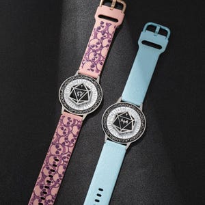 May include: Two wristwatches with unique designs. One watch has a pink strap with skull patterns, the other has a light blue strap. Both watches feature a black and white face with a geometric design and the text "ROLL HIGHORDIE".