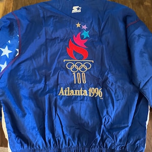 Puede incluir: Chaqueta azul Starter con el logo de los Juegos Olímpicos de Atlanta 1996 en la espalda. La chaqueta tiene un estampado de estrellas blancas y azules en la manga izquierda y un logotipo de Starter en el cuello. La chaqueta es de material ligero y brillante.