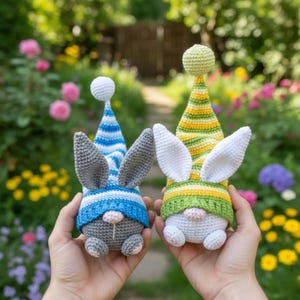 May include: Two handmade crochet bunny gnomes. One gnome has a blue and white striped hat and gray ears. The other has a yellow, green, and white striped hat and white ears. Both have a pink nose and are sitting.