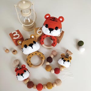 May include: Three crocheted tiger toys with wooden rings. One tiger is attached to a wooden bead and crocheted bead necklace with a clip.