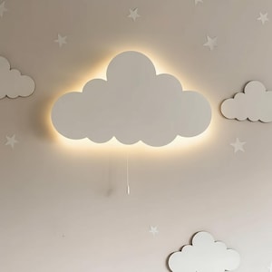 Peut inclure: Une applique murale en forme de nuage blanc avec une lueur chaude, dotée d'un interrupteur à cordon. La lumière est entourée d'autres décorations en forme de nuages et d'étoiles sur un mur de couleur neutre, créant un thème de chambre d'enfant.