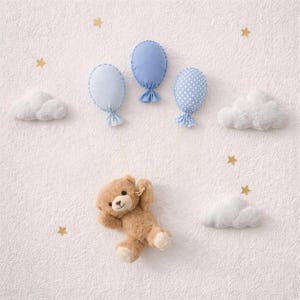 Puede incluir: Decoración de pared para guardería con un oso de peluche suspendido de tres globos de tela azul y nubes blancas esponjosas. Estrellas doradas adornan el fondo texturizado blanquecino.