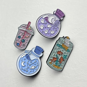 Peut inclure: Quatre épingles émaillées aux motifs fantaisistes. L'une représente un bubble tea avec des planètes, une autre une potion violette avec des fantômes, une troisième une potion bleue avec des constellations et la dernière un bocal avec un chat et des poissons.