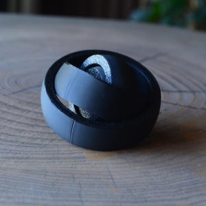 Peut inclure: Un objet rond noir multi-couches avec une surface texturée. L'objet est fait d'un matériau souple et flexible et semble être un jouet anti-stress.