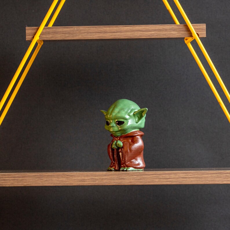 May include: A green and brown Yoda figurine standing on a wooden shelf with yellow rope hanging from the ceiling.