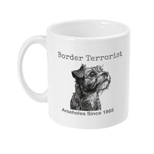 May include: White ceramic mug with a black and white illustration of a Border Terrier dog. The mug has the text "Border Terrorist" and "Arseholes Since 1865" printed on it.