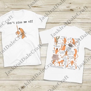 Puede incluir: Dos camisetas blancas con gráficos humorísticos. Una camiseta dice "don't piss me off" con un personaje de dibujos animados. La otra camiseta tiene varios personajes y frases como "It's making me mad."