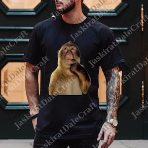 Peut inclure: T-shirt noir avec un motif détaillé d'un singe pensif. Le singe a un pelage brun et beige. Le t-shirt est de style col rond.